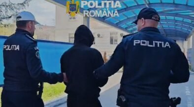 Two Romanian police officers escort a hooded person outdoors under a blue canopy labeled Politia Romana.