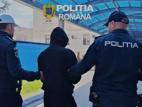 Two Romanian police officers escort a hooded person outdoors under a blue canopy labeled Politia Romana.