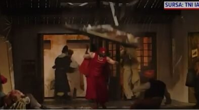 People rush through a doorway as debris falls from a damaged interior during an explosion scene, with a person in red clothing center-stage guarding the exit.