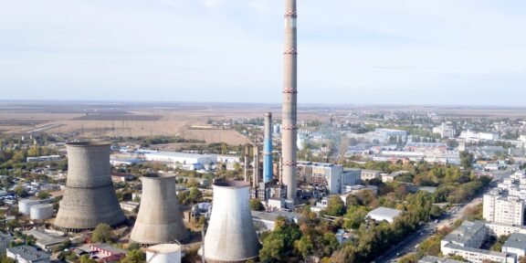 Aerial view of a large industrial plant with tall smokestack and several cooling towers near a town horizon