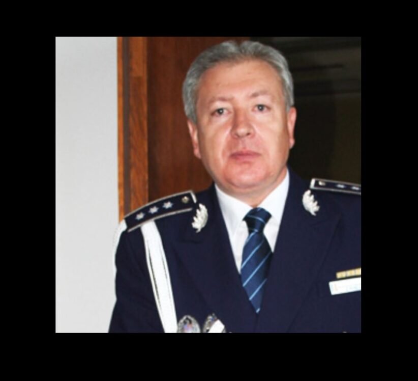 Middle-aged man in formal max blue military uniform with epaulets, medals, and striped tie, standing indoors.