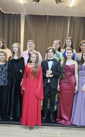 A group of young people in formal wear posing on a stage with dark curtains in the background.