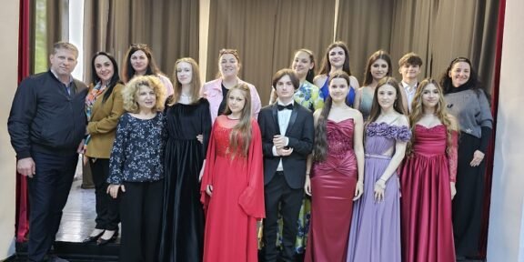 A group of young people in formal wear posing on a stage with dark curtains in the background.