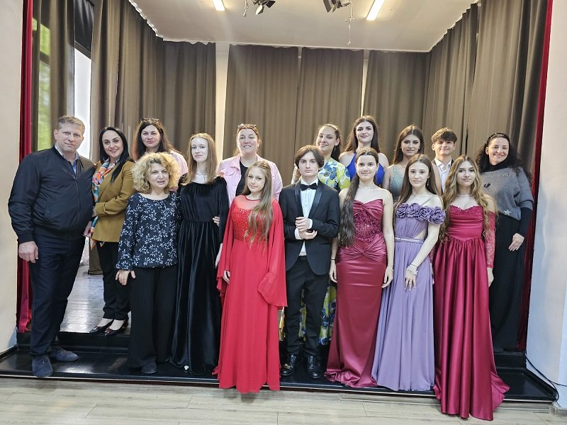 A group of young people in formal wear posing on a stage with dark curtains in the background.