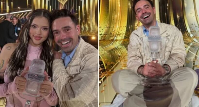 Woman in pink holds a clear Eurovision trophy while a smiling man stands beside her in a glittering backstage area.