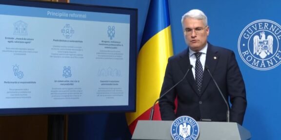 Romanian government official at a lectern with the national flag and Government of Romania insignia, delivering a presentation with a slide titled 'Principiile reformei'