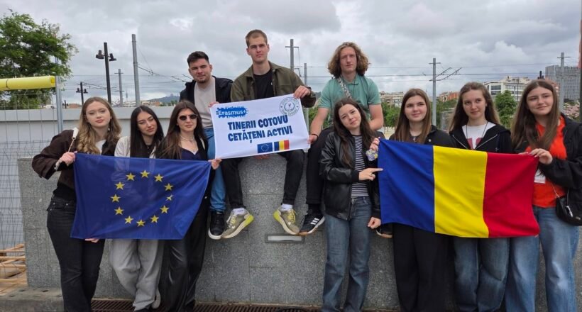 Group of diverse young students on a rooftop, holding the EU flag and the Romanian flag with an Erasmus banner saying active citizens.