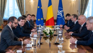 Diplomatic meeting at a long table with European Union, Romanian, and NATO flags behind, officials seated on both sides.