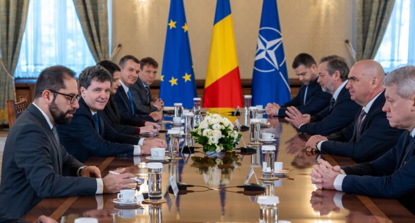 Diplomatic meeting at a long table with European Union, Romanian, and NATO flags behind, officials seated on both sides.