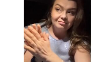 Woman with long hair smiling while clapping her hands, wearing a light blue top.