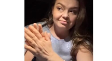 Woman with long hair smiling while clapping her hands, wearing a light blue top.