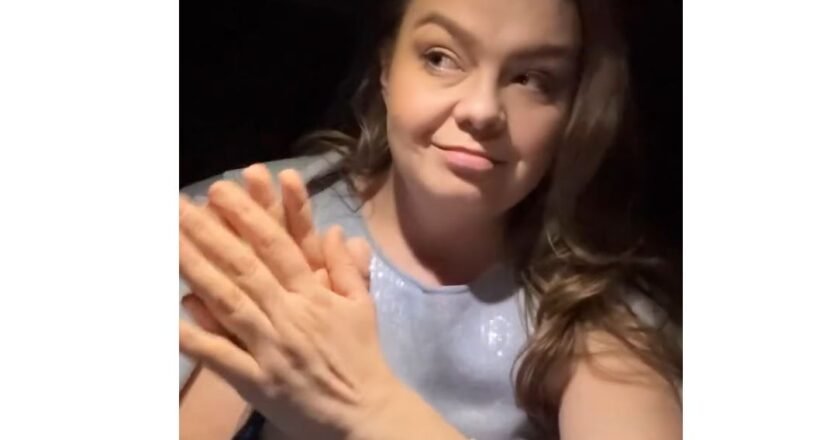 Woman with long hair smiling while clapping her hands, wearing a light blue top.