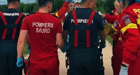 Emergency responders in red and dark uniforms gather around a patient on a wheeled stretcher outdoors during a rescue.