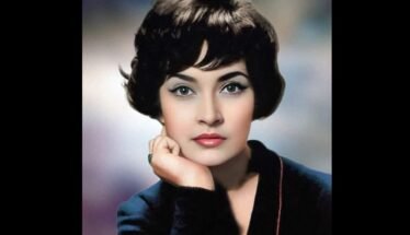 Vintage studio portrait of a woman with short dark hair, resting her chin on her hand in a blue blazer.