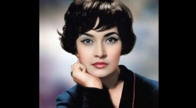 Vintage studio portrait of a woman with short dark hair, resting her chin on her hand in a blue blazer.
