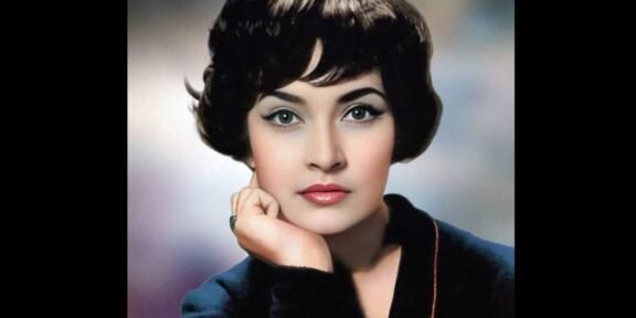Vintage studio portrait of a woman with short dark hair, resting her chin on her hand in a blue blazer.