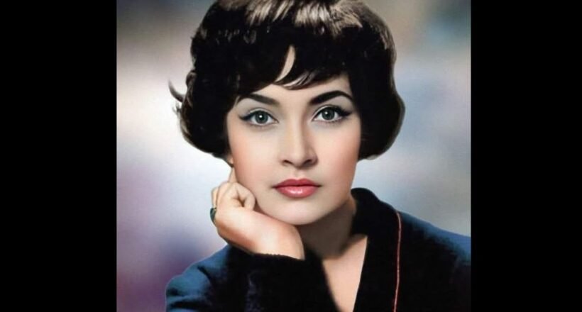 Vintage studio portrait of a woman with short dark hair, resting her chin on her hand in a blue blazer.