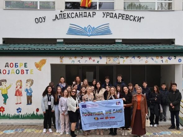 Group of students and teachers posing outside a school, holding a banner that reads 'TOGETHER, WE CAN!', with colorful wall art and the school's façade in the background.
