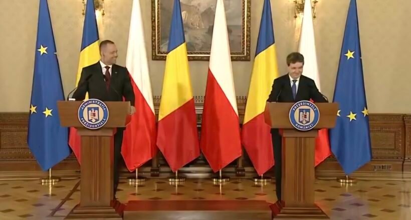 Two men in suits speak at podiums in a formal government room, with EU and Romanian flags behind them.