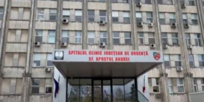 Front entrance of a large hospital building with stairs and glass doors, sign reads 'Spitalul Clinic Judetean de Urgenta Sf. Apostol Andrei'