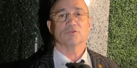 Man in a pinstripe suit being interviewed, speaking into a microphone.