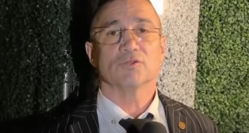 Man in a pinstripe suit being interviewed, speaking into a microphone.