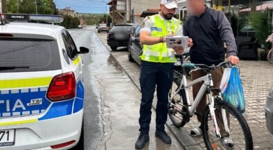 Police officer in a high-visibility vest analyzes a document with a man beside a white bike on a wet street by a police car.