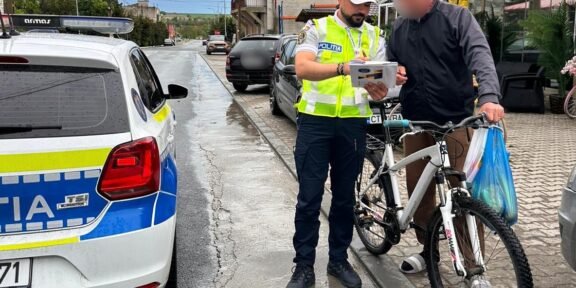 Police officer in a high-visibility vest analyzes a document with a man beside a white bike on a wet street by a police car.