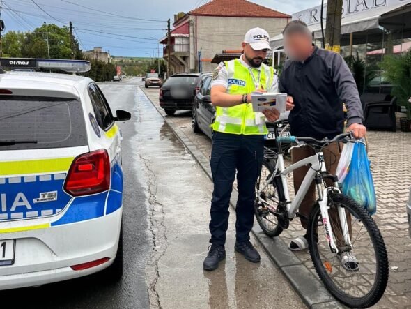 Police officer in a high-visibility vest analyzes a document with a man beside a white bike on a wet street by a police car.