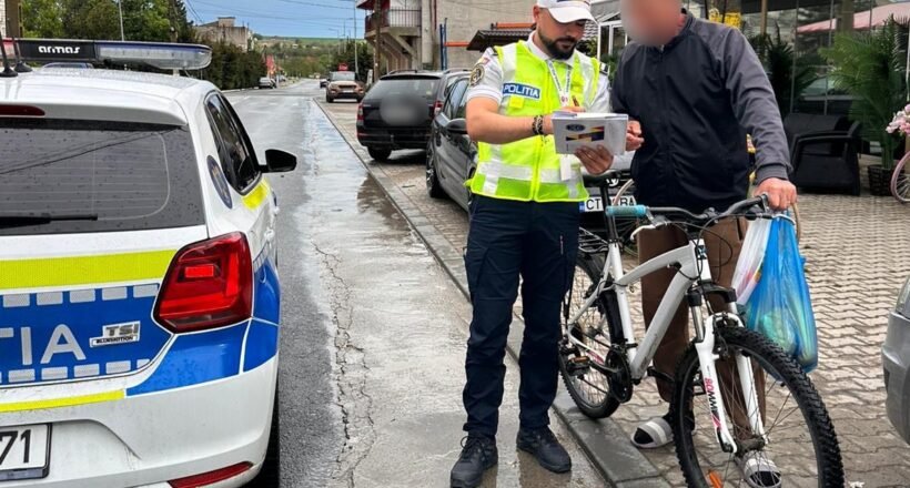 Police officer in a high-visibility vest analyzes a document with a man beside a white bike on a wet street by a police car.