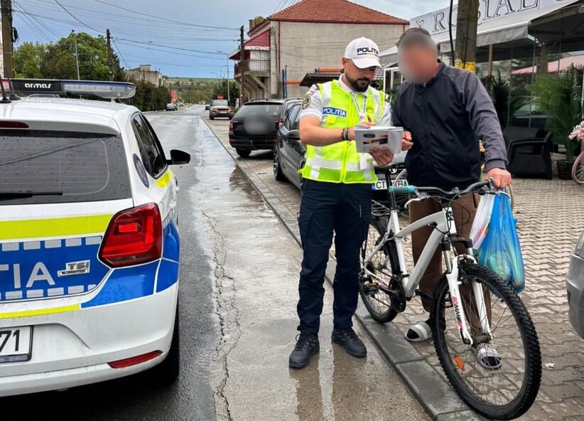 Police officer in a high-visibility vest analyzes a document with a man beside a white bike on a wet street by a police car.