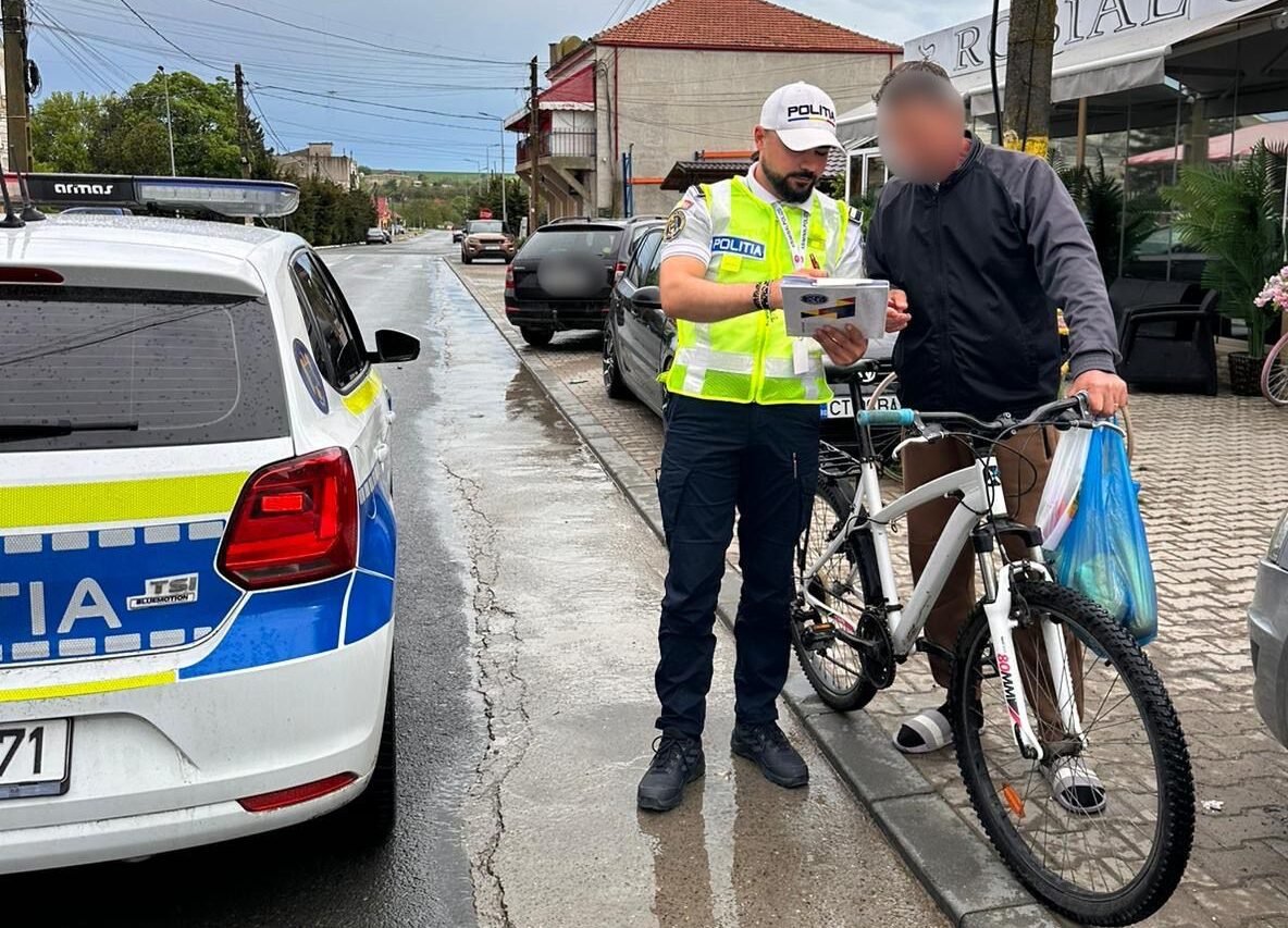 Police officer in a high-visibility vest analyzes a document with a man beside a white bike on a wet street by a police car.
