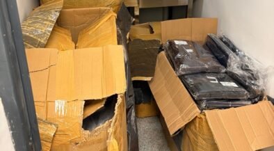 Overflowing storage closet with torn cardboard boxes and sealed black bags.