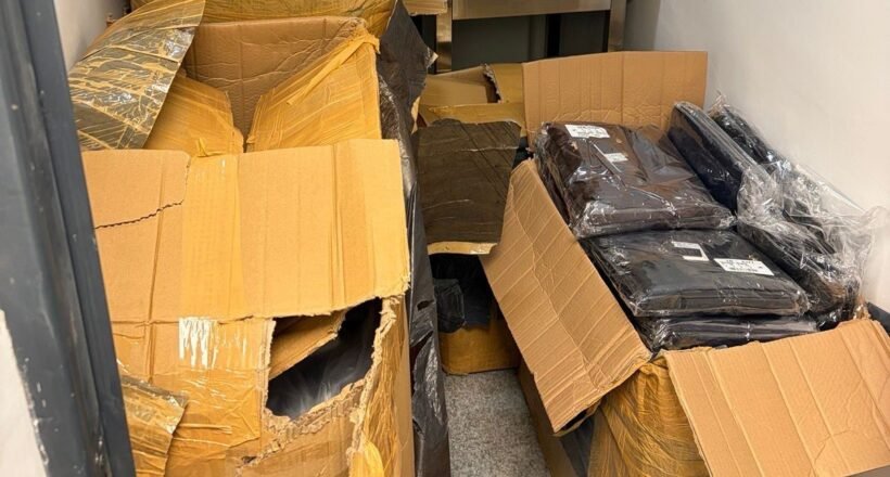 Overflowing storage closet with torn cardboard boxes and sealed black bags.