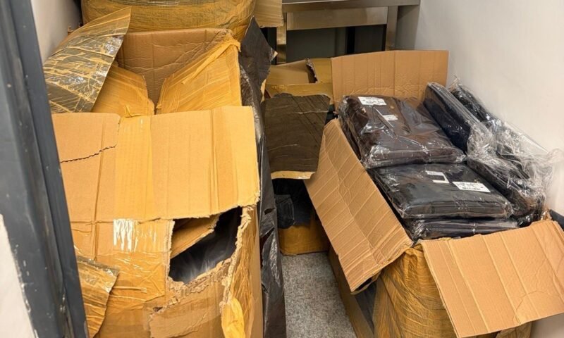 Overflowing storage closet with torn cardboard boxes and sealed black bags.