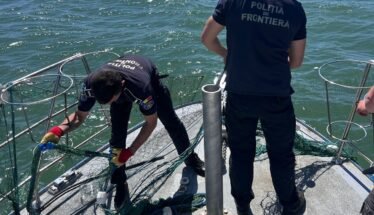 Border police officers on a boat untangling a fishing net near the railing, with open water in the background on a sunny day