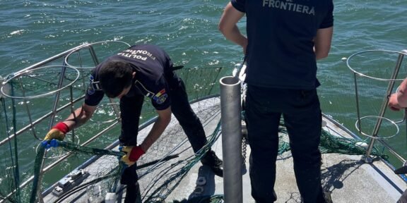 Border police officers on a boat untangling a fishing net near the railing, with open water in the background on a sunny day