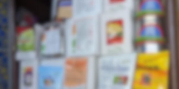 Blurred display shelf holding multiple white brochures and colorful packaging on the right side.
