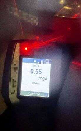 Breathalyzer device displaying a reading of 0.55 mg/L on the screen with a red indicator light nearby, blurred background.