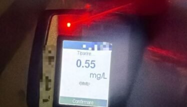 Breathalyzer device displaying a reading of 0.55 mg/L on the screen with a red indicator light nearby, blurred background.