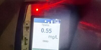 Breathalyzer device displaying a reading of 0.55 mg/L on the screen with a red indicator light nearby, blurred background.