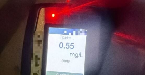 Breathalyzer device displaying a reading of 0.55 mg/L on the screen with a red indicator light nearby, blurred background.