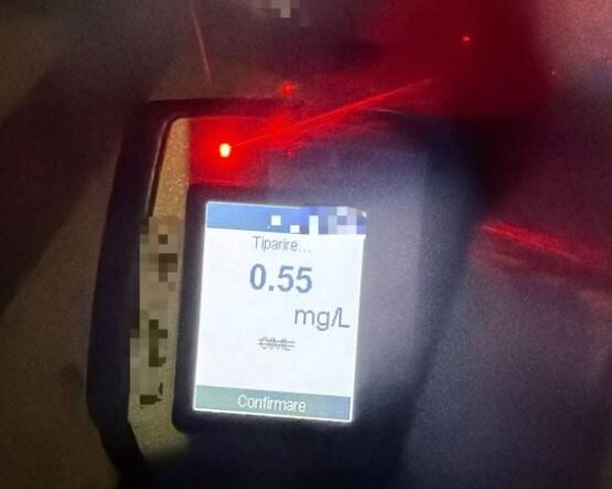 Breathalyzer device displaying a reading of 0.55 mg/L on the screen with a red indicator light nearby, blurred background.
