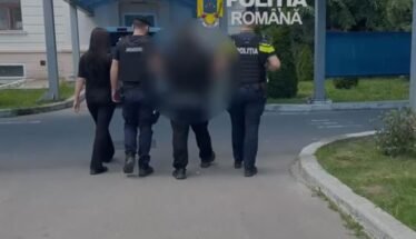 Police officers escorting a blurred person down a street near a building entrance with a blue canopy; 'Politia Romana' emblem visible