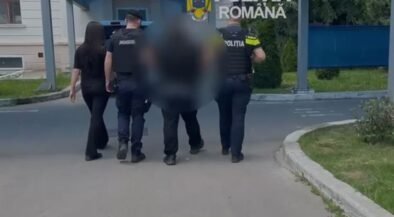 Police officers escorting a blurred person down a street near a building entrance with a blue canopy; 'Politia Romana' emblem visible