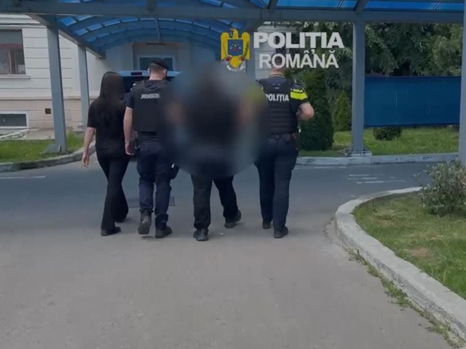 Police officers escorting a blurred person down a street near a building entrance with a blue canopy; 'Politia Romana' emblem visible