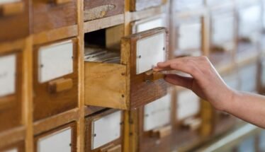 Hand pulling open a small wooden filing cabinet drawer with a label card inside.