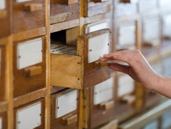 Hand pulling open a small wooden filing cabinet drawer with a label card inside.