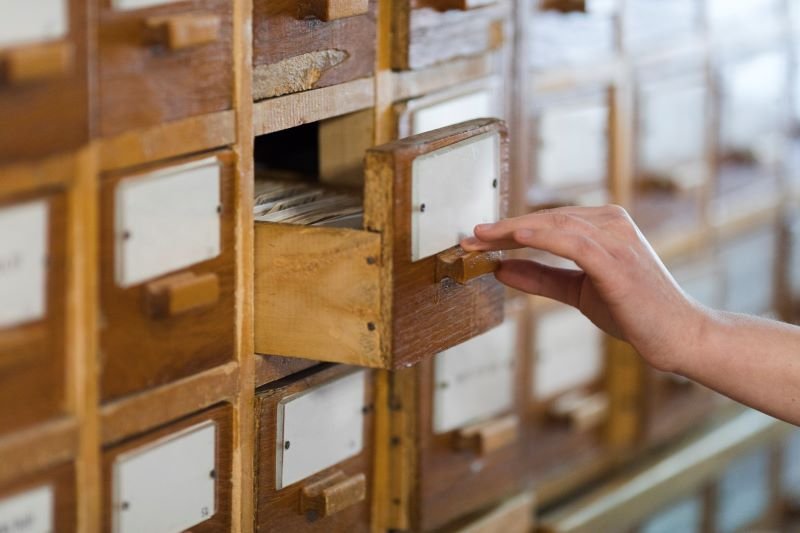 Hand pulling open a small wooden filing cabinet drawer with a label card inside.