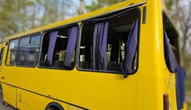 Yellow school bus with open windows and purple curtains, parked outdoors